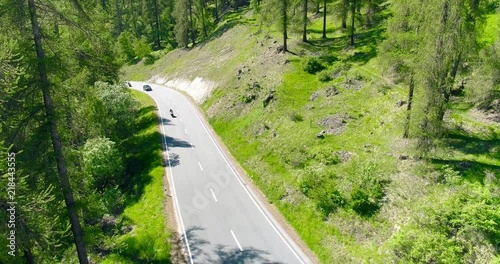 Cars and moto move at highway bridge road in mountains above valley village morning aerial 4k. Fly above traffic over hill town Europe sun shine. Motorway vehicles pass scenic Italian Alps landscape