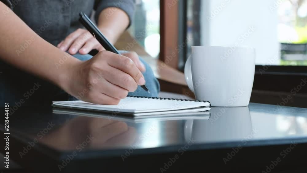 A woman's hand writing down on a white blank notebook on table A woman's hand writing down on a white blank notebook on table