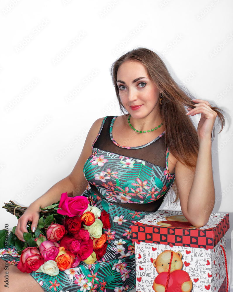A happy, beautiful woman is sitting with a gift box and a bouquet of roses, on a white background. Valentine's Day. A happy, beautiful woman is sitting with a gift box and a bouquet of roses, on a white background. Valentine's Day.