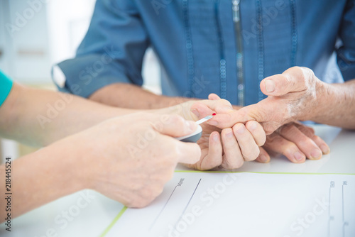 Nurse's hands Using Glucometer On Senior female Patient's Finger