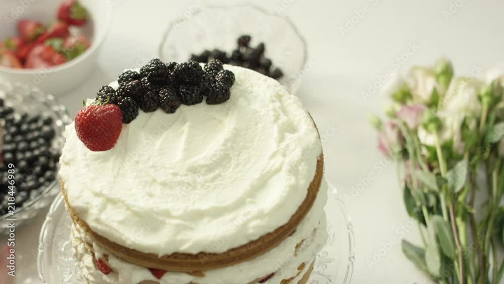 Woman places strawberries on top of beautiful naked cake in a bright kitchen