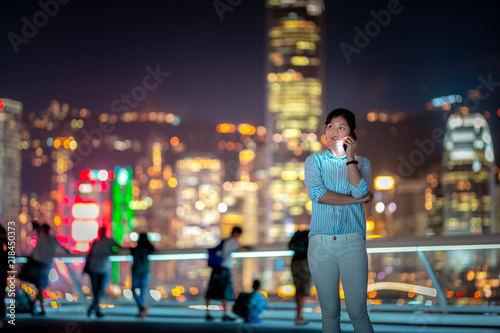 Woman using smartphone at night with Victoria Horbor in background photo