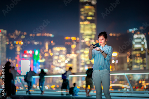 Photography Woman using smartphone at night with Victoria Horbor in background