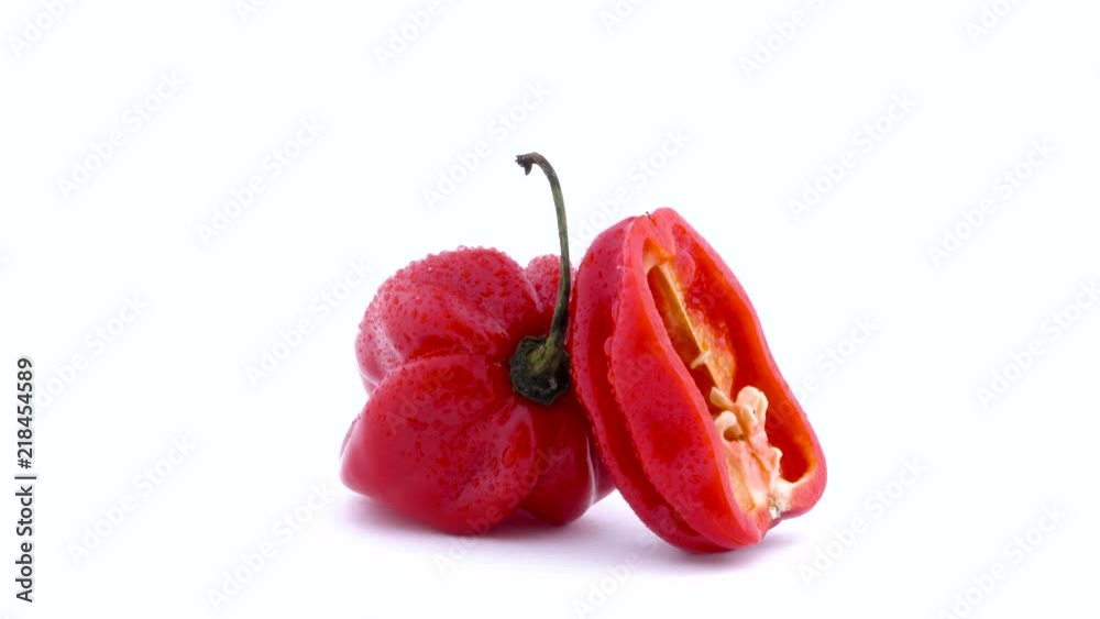 One whole and one half of red habanero chili pepper with water drops. Rotating on the turntable isolated on the white background. Close-up. Macro. One whole and one half of red habanero chili pepper with water drops. Rotating on the turntable isolated on the white background. Close-up. Macro.
