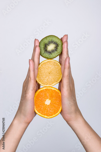 Female hands holding a lemon, orange, kiwi on a white background