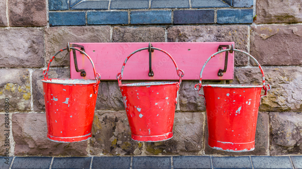Three old hanging red metal fire buckets on a heritage railway station in Wales UK Three old hanging red metal fire buckets on a heritage railway station in Wales UK