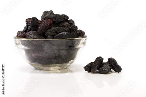 Black raisins in a glass bowl isolated on white background