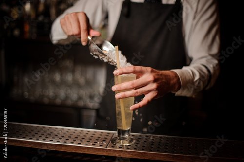 Barman adding ice into a glass with sour summer cocktail