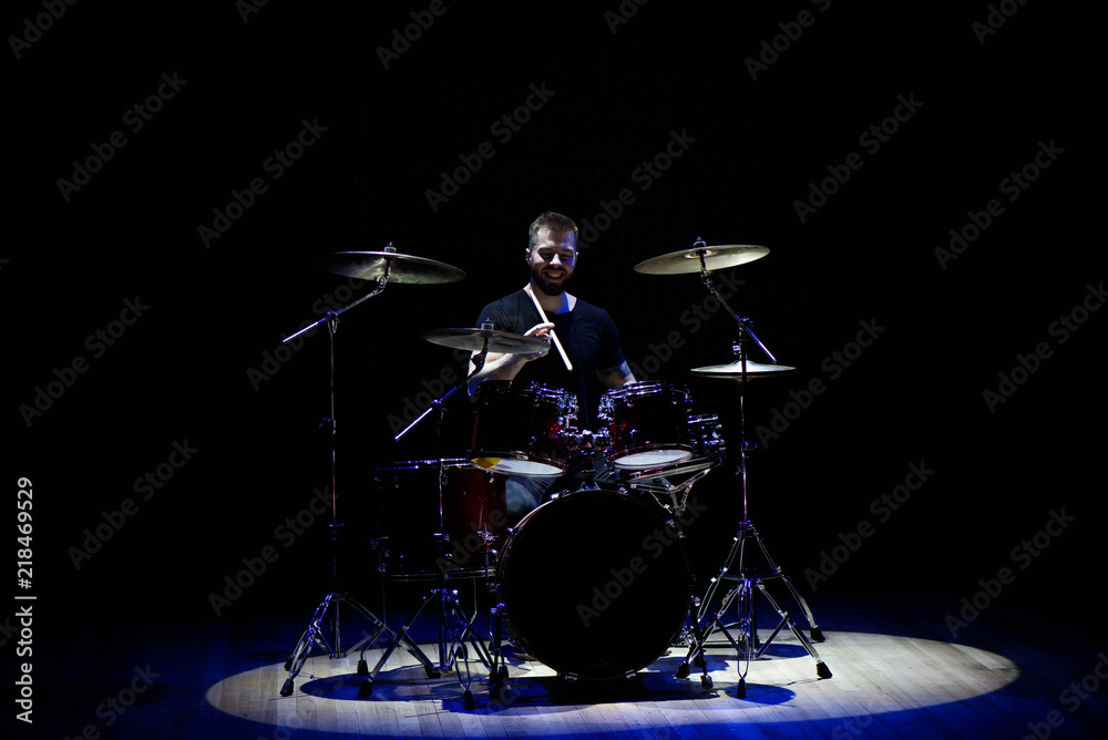 Fototapeta premium Drummer in a cap and headphones plays drums at a concert under white light in a smoke