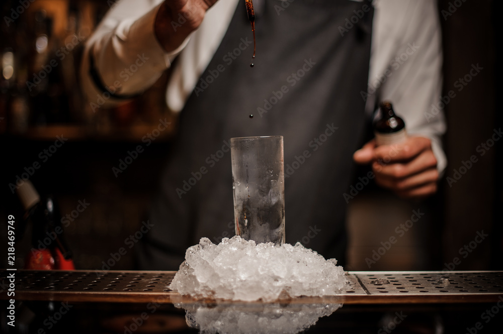 Bartender adding some drops of brown bitter into a cocktail glass