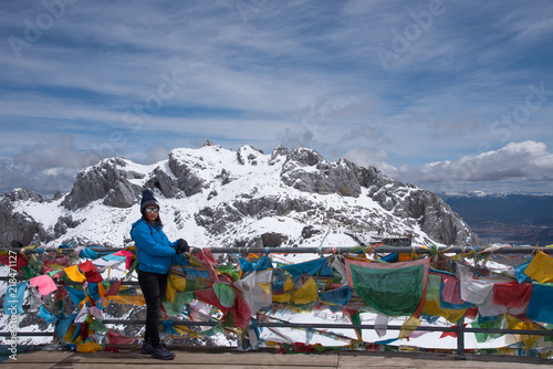 Tourist woman standing and enjoy view of beautiful snow mountains name "Shika snow mountains" on the top in Shangri-La, Yunan, China, acting and happy with cool weather on peak.