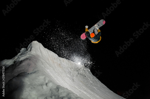 snowboarder idemonstrates a beautiful jump against the background of snow mountains at night