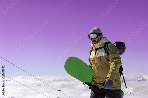 man with a green snowboard in his hand walking along the snow to a mountain lift