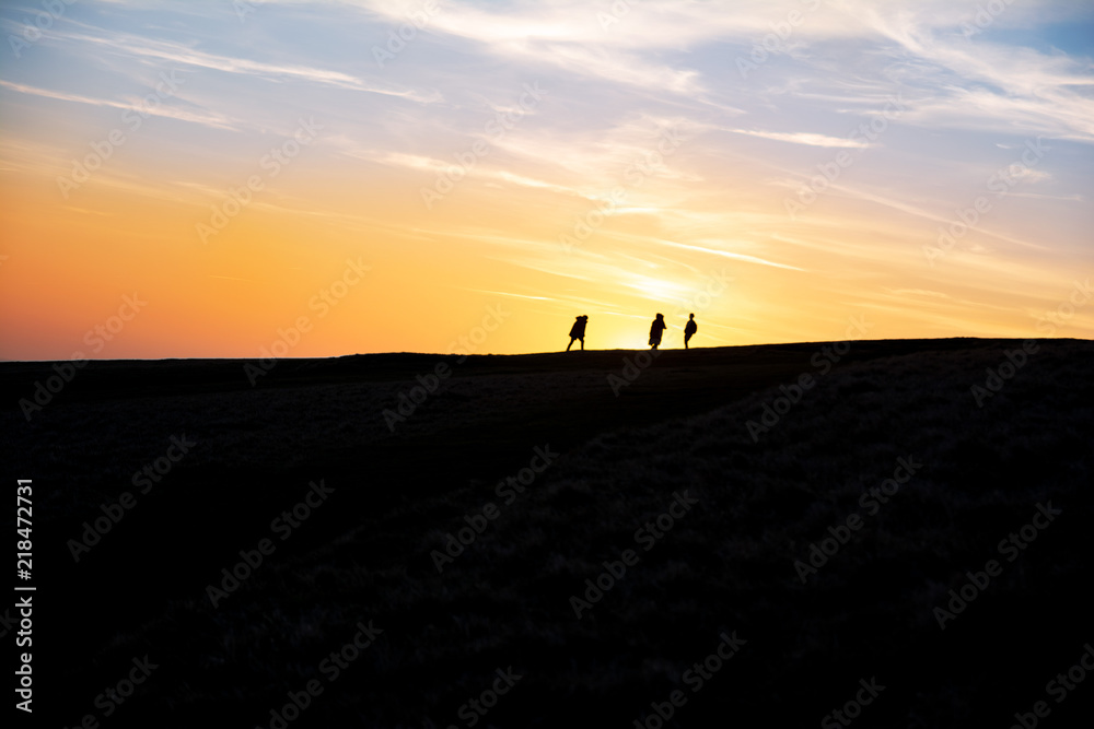 People walking on a hill in front of a beautiful sunset