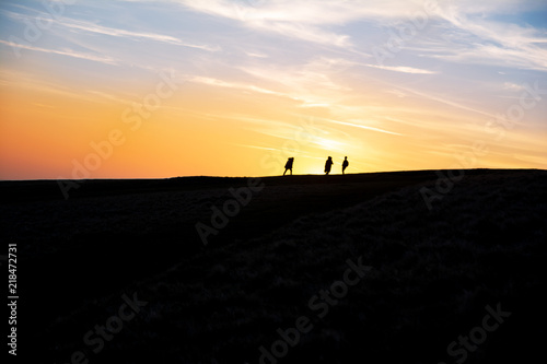 People walking on a hill in front of a beautiful sunset