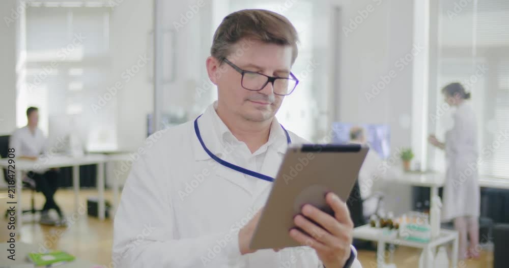 Successful man doctor with eyeglasses using video calls on tablet while working in modern clinic. Doctor gives advises to patient on video link Successful man doctor with eyeglasses using video calls on tablet while working in modern clinic. Doctor gives advises to patient on video link