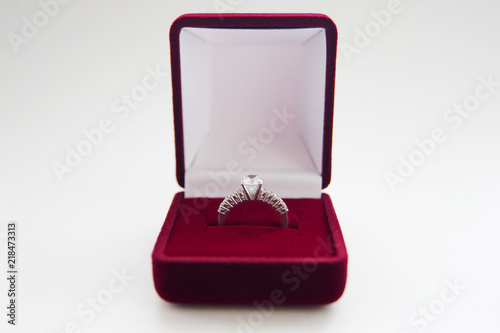 Front view of beautiful wedding ring with precious stone in red velvet gift box on white background. For present and marriage proposal.