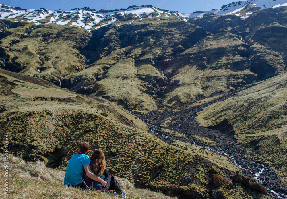Love in the nature. A couple sitting in the mountains looking at beautiful surrounding. A guy is hugging a girl. A lonely couple in the nature with no people around. Iceland.