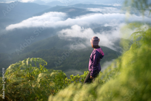 Tourist woman standing on peak of mountains and enjoy view with beautiful mist and sunrise from her success at Gunungsilepat mountains, Yala province south of Thailand.