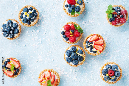 Delicious tartlets or cake with mixed berry on blue background from above. Summer pastry desserts.