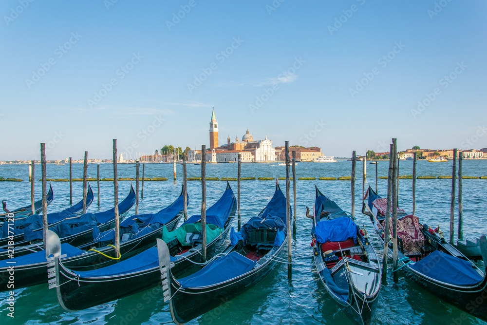 Pack of gondolas docked in Saint Mark's square Venice, in the background it can be seen a church with a bell tower 