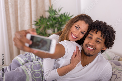 Beautiful young couple taking a selfie in bed