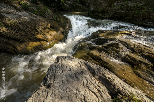 Wide angle shot of mountain river with a waterfall flowing between rocky coasts. Expressive foreground. Taken from low point of view at sunny spring day at Carpathian mountains. Natural background. 