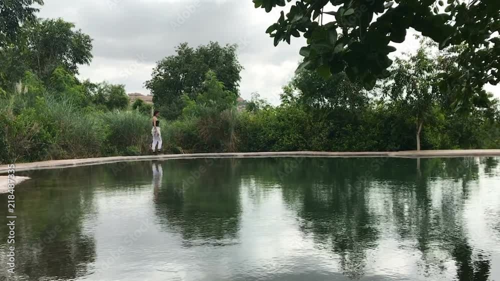 Girl walking around natural made pool in rocky tropical surrounding in Hampi, India