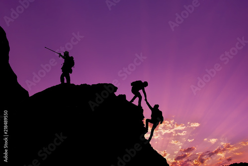 Hikers climbing on rock, mountain at sunset, one of them giving hand and helping to climb.Teamwork , Helps ,Success, winner and Leadership concept .
