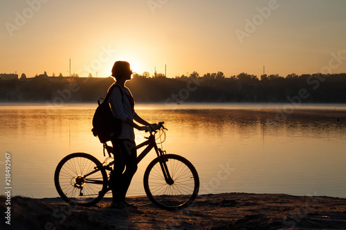 A girl with a bike near the lake in the summer morning