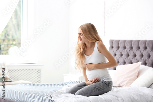 Young pregnant woman suffering from pain in bedroom. Gynecology concept