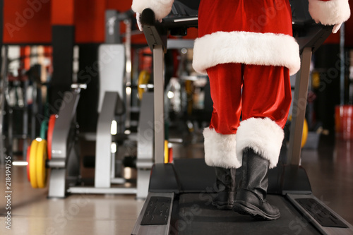 Authentic Santa Claus training on treadmill in modern gym, focus on legs