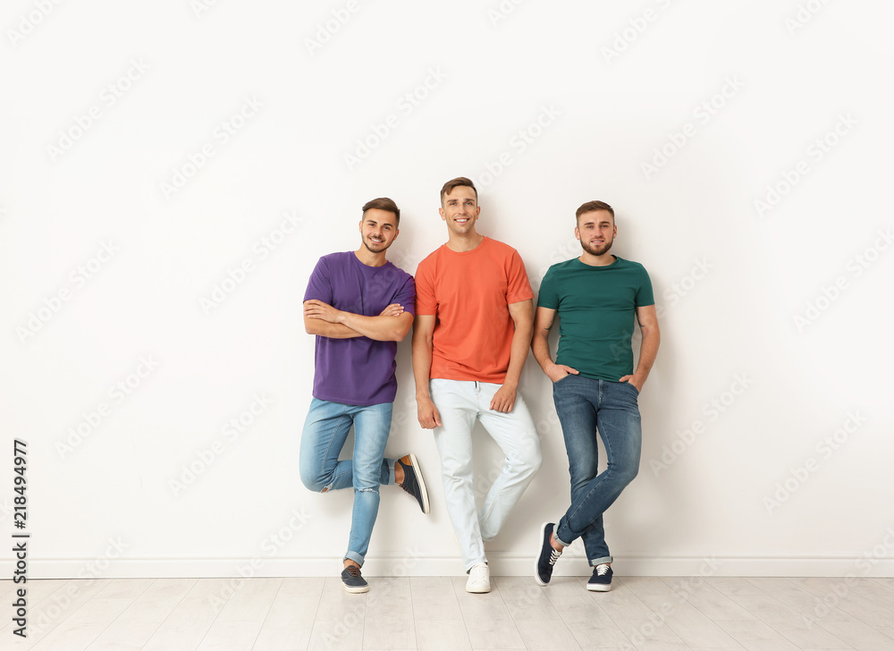 Fototapeta premium Group of young men in jeans and colorful t-shirts near light wall