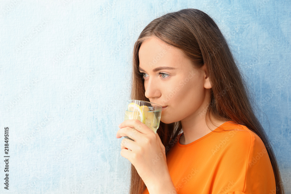 Young woman drinking lemon water on color background Young woman drinking lemon water on color background