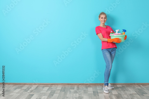 Woman with cleaning supplies near color wall