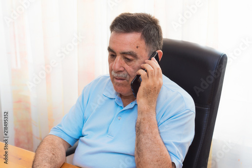 Cheerful Senior Man working on laptop while talking on the phone