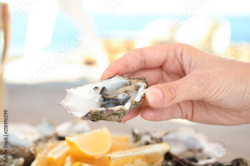 Woman holding fresh oyster over plate, focus on hand