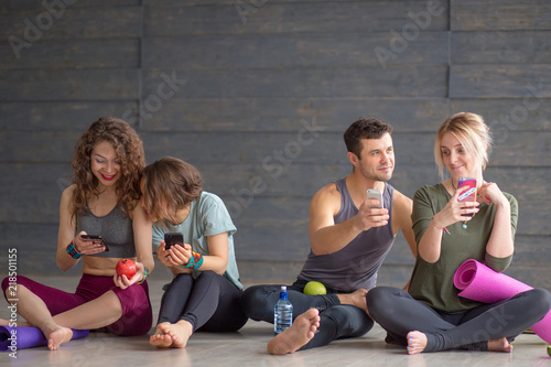 Cheerful fit young co-workers in sportswear having rest and drinking water after workout on floor before going home. People, body shape, health, wellbeing and active lifestyle concept.