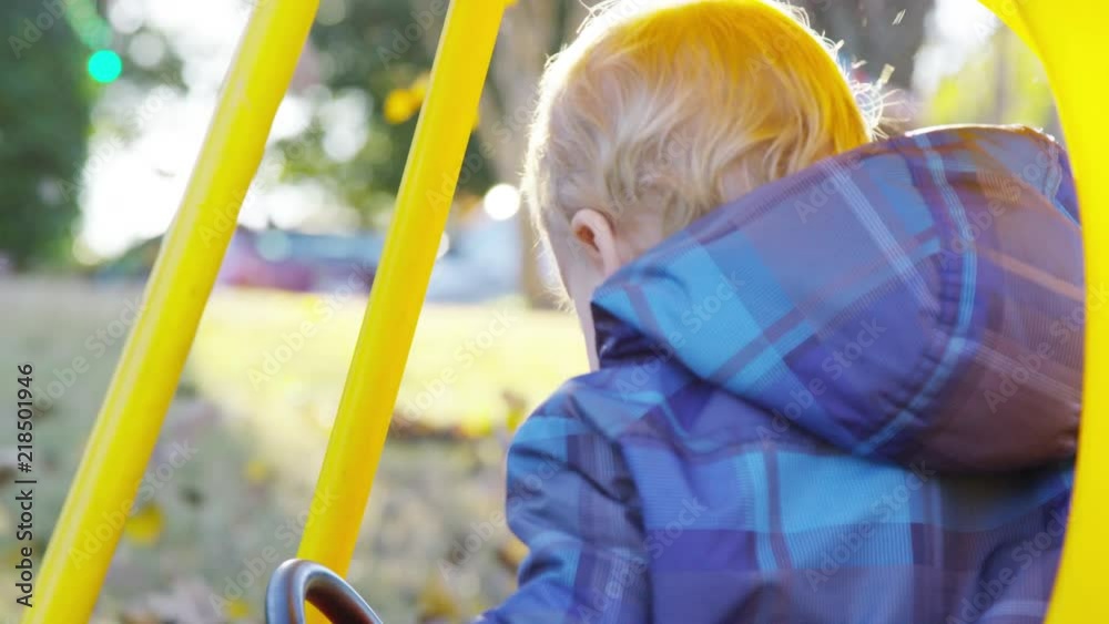 Leaves fall around toddler as he get into a toy car