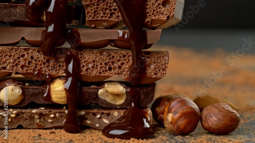 Melted chocolate pouring over heap of broken pieces chocolate and nuts. Slider shot. UHD, 4K
