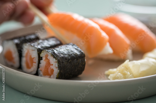 Woman eating Japanese salmon Nigiri and Maki Sushi with pickled ginger and wooden chopsticks from porcelain plate