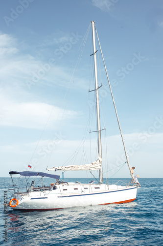 Floating yacht with sails down in calm sea. A boat lowered the sails and anchored near the coast