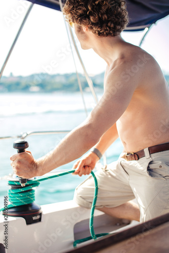 sail boat red-haired young captain navigating the boat, halliard fall off by pull the rope with tackle in the sea on blue sky holiday. photo