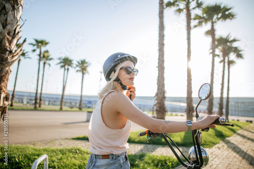 people, transport, technology, travel and vacation concept - outdoor portrait of pretty cute tourist woman smiling beside her electric bike in park with palms in summer morning. photo