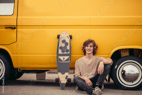 Young hipster guy sitting next his yellow car during road trip photo