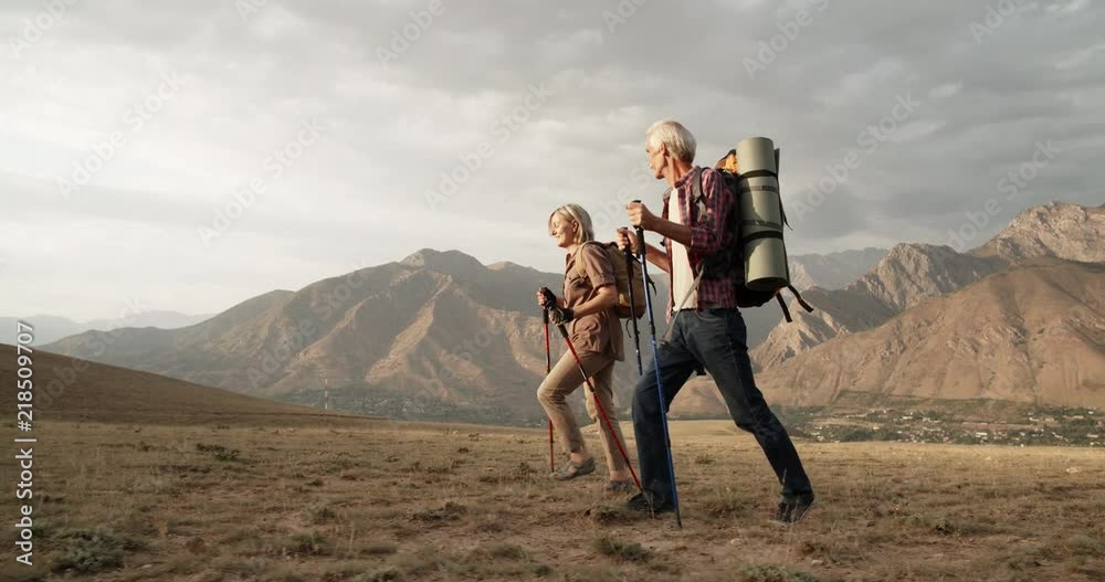 Old caucasian couple hiking, trekking in mountains with backpacks, enjoying their adventure - tourism concept 4k