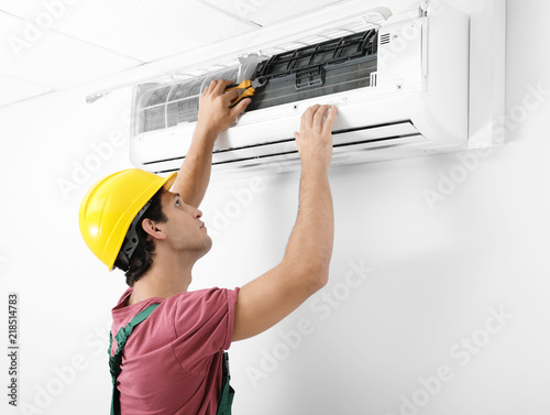 Male technician checking and repairing air conditioner indoors