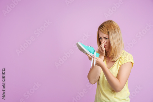 Young woman with stinky shoe on color background. Air freshener