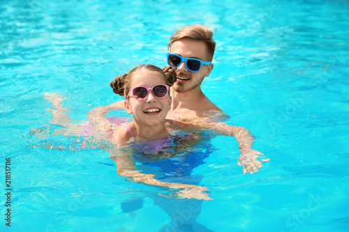 Young man teaching his daughter to swim in pool