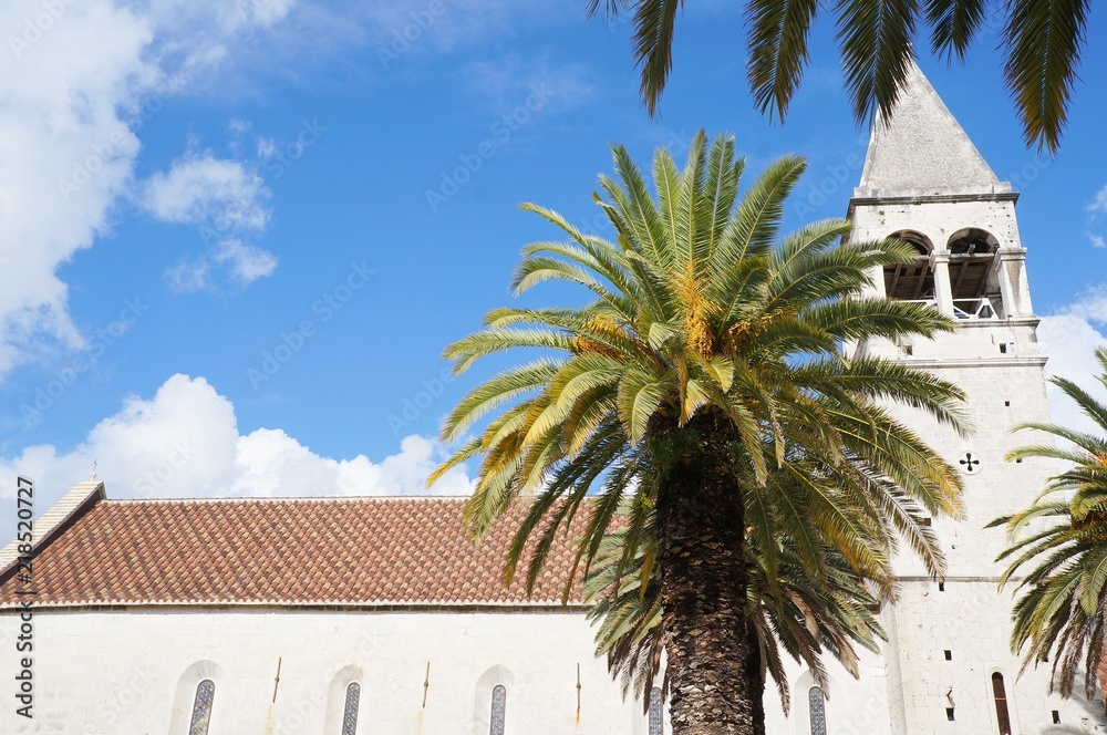 Saint Dominican convent and church in Trogir, Croatia, surrounded by palm trees
